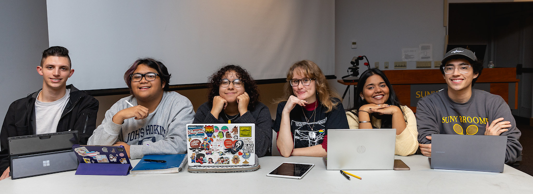 Students Seated at a table with laptops open.